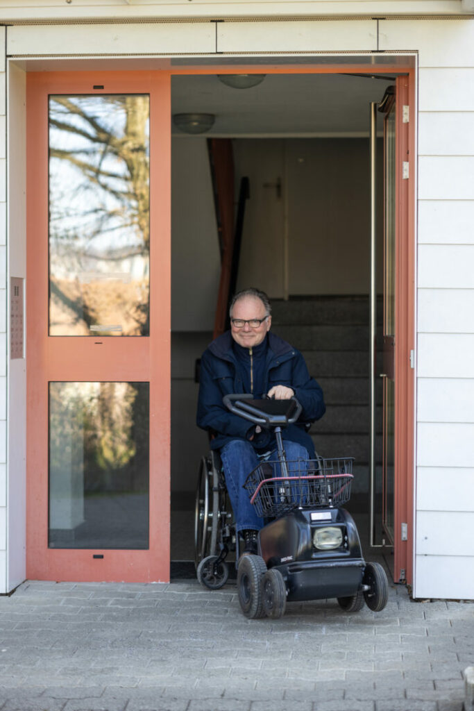 Alex Oberholzer auf Rollstuhl im geöffneten Eingang zu seinem Wohnblock.